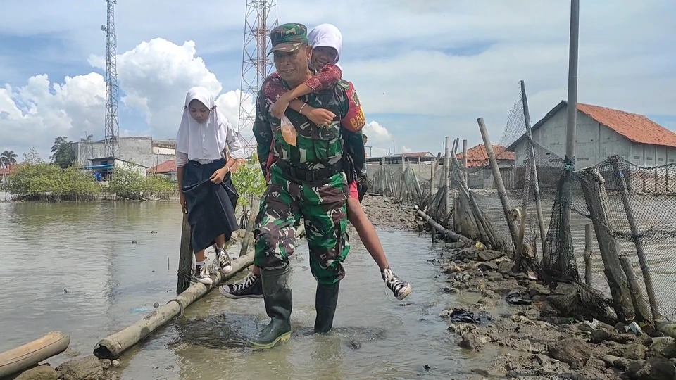 Babinsa TNI membantu siswa di Indramayu melewati jalan yang rusak saat pulang sekolah. (Beritasatu/Andrian Supendi)