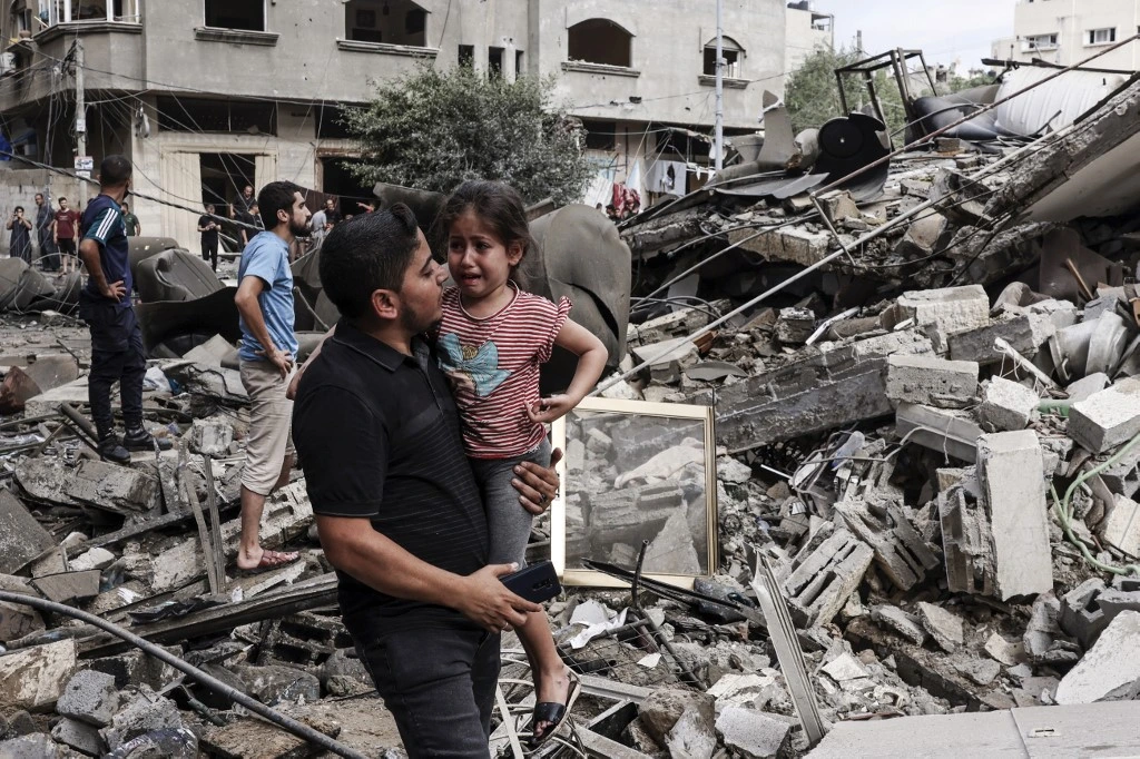 Image Credit AFP - Seorang pria menggendong anak kecil di tengah kehancuran di kota Gaza yang diakibatkan serangan Israel.