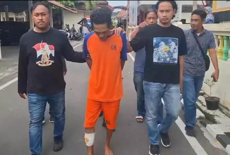 Image Credit Istimewa - Eko Fitrianto, pelaku mutilasi, saat dibawa oleh petugas kepolisian setelah berhasil ditangkap. Pelaku yang merupakan rekan kerja korban terpaksa ditembak kaki kanan setelah berusaha melawan petugas saat penangkapan di rumahnya di Jombang.